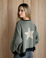 Buzo de punto color verde oliva con diseño de estrella grande en color beige en la espalda. Presenta un corte holgado, cuello redondo y terminaciones en color negro en el cuello, puños y ruedo.