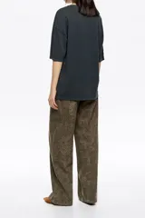 Pantalón largo de algodón, color verde militar, con corte wide leg, tiro bajo y diseño de cinco bolsillos. Presenta un patrón estampado en relieve tipo piel de serpiente y cortes horizontales en las piernas.