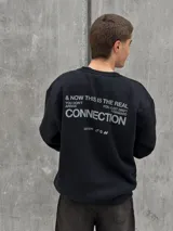 Buzo negro de corte holgado con cuello redondo y puños acanalados. Estampado frontal con la palabra "OSTEN" y la frase "NOT WHERE YOU'RE FROM A MINDSET OF BECOMING" en color blanco.