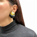 Caravanas artesanales de diseño italiano, compuestas por una pieza superior circular con textura dorada y una pieza inferior en forma de media luna de color negro brillante. Elaboradas en resina de alta calidad con sistema de ajuste mediante clip.