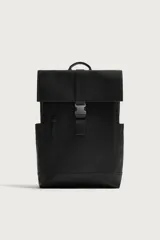 Mochila de diseño minimalista en acabado engomado color negro. Cuenta con compartimento principal con cierre de solapa y hebilla de liberación rápida, bolsillo frontal con cierre, compartimento interno para dispositivos electrónicos y espalda acolchada con banda de sujeción para equipaje.