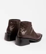 Bota corta de cuero vacuno con acabado metalizado y textura de reptil. Presenta punta fina, cierre lateral interno y taco cuadrado de madera.