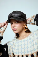 Boina estilo cap con visera, confeccionada en cuero vegano de color marrón oscuro. Presenta un diseño estructurado con costuras visibles en la parte superior.