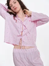 Camisa de dormir de popelina de algodón, con estampado de rayas verticales y pequeños motivos geométricos. Presenta cuello camisero, mangas largas y cierre frontal mediante lazos ajustables.