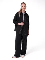 Camisa de denim gris con costuras en contraste, corte oversized, cuello camisero, cierre frontal con botones metálicos y bolsillos dobles en el pecho.