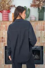 Camisa negra de manga larga con cuello clásico, cierre frontal con botones a presión y dos bolsillos de parche en el pecho. Presenta apliques de strass plateados en la parte superior delantera.