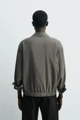 Sobrecamisa de corte cropped confeccionada en tejido ligero con algodón, con estampado de cuadros pequeños en tonos oscuros. Presenta cuello solapa, cierre frontal de botones, manga larga con puño abotonado y bajo con elástico en la espalda.
