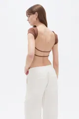 Top ajustado de poliéster color marrón, con mangas cortas, cuello redondo a la base y diseño abierto en los laterales con tiras cruzadas.