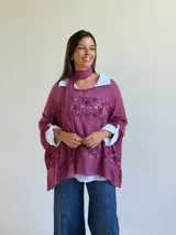 Sweater de punto magenta con diseño holgado, cuello redondo y detalles de encaje floral aplicado en el frente. Incluye una bufanda tipo choker integrada del mismo tejido.