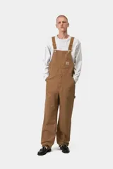 Mameluco Carhartt WIP modelo Bib Overall, de color negro, con múltiples bolsillos frontales, tirantes ajustables con hebillas metálicas y el parche con el logotipo de la marca en el bolsillo del peto.