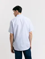 Camisa blanca con estampado de micro lunares celestes, de corte clásico, manga corta, cuello abotonado y bolsillo en el pecho.