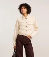 Campera color crudo de manga larga, confeccionada en sarga de algodón, con cuello inglés, abotonada al frente, bolsillos con solapa en el pecho y costuras contrastantes en color marrón.