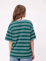 Remera de corte holgado con diseño de rayas horizontales en tonos beige, rosa y verde oliva. Presenta cuello redondo, mangas cortas y un bolsillo frontal pequeño con el logo de la marca.