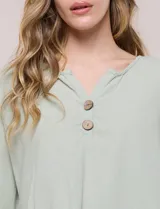 Blusa Erika de algodón con estampado de rayas en tonos azules, rosados y amarillos. Presenta cuello redondo con escote en V y botones frontales, mangas cortas decoradas con una fila de botones en los laterales y dobladillo asimétrico.