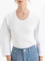 Top de tejido de punto acanalado en color blanco, con cuello redondo y mangas tres cuartos de tela plana con volumen. Presenta un diseño ajustado al cuerpo que contrasta con la estructura de las mangas.