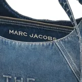 Cartera de hombro tipo slouchy de Marc Jacobs modelo The Sack Bag, confeccionada en denim azul con el nombre de la marca y del modelo estampado en color blanco en el lateral. Posee diseño holgado y correa integrada con detalles de tiras colgantes.