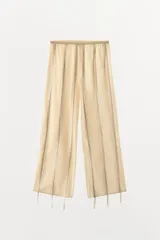 Pantalón de tiro medio confeccionado en algodón, con cintura elástica y diseño de corte recto. Presenta aplicaciones verticales de cintas o lazadas a lo largo de las piernas.