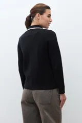 Chaqueta tejida de punto color naranja, con cuello camisero, cierre frontal de botones y dos bolsillos frontales con solapa. Presenta detalles de bordado en contraste en el cuello y los bolsillos.