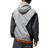 Campera rompevientos con capucha Nike Jordan, diseño color block en tonos gris claro, gris oscuro y negro. Presenta cierre frontal completo, bolsillos laterales y logo Jumpman bordado en el pecho.