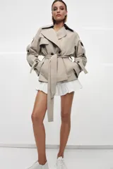Trench corto de corte oversize confeccionado en mezcla de algodón con acabado repelente al agua. Presenta cuello solapa, cierre frontal con botones, mangas largas con trabillas ajustables y cinturón a tono con lazada en la cintura.