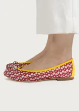 Bailarina de diseño artesanal confeccionada en rejilla bordada con patrón floral en tonos rojizos sobre fondo claro. Presenta ribetes y talón en color amarillo vibrante, con un detalle de media esfera metálica dorada en la puntera y suela plana.
