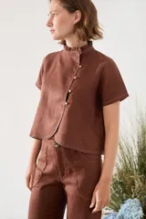 Blusa de lino verde de manga corta y corte recto, con cuello alto con volado y cierre frontal cruzado con botoncitos dorados.