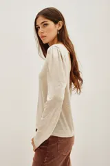Remera de viscosa en color beige, de manga larga con detalle de frunces en los hombros y un pronunciado escote en la espalda con tira horizontal.