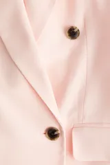 Blazer rosado de doble botonadura levemente largo con hombreras, solapas de muesca, bolsillos delanteros ribeteados con solapa y forro interior.