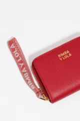 Billetera compacta de estructura rígida en piel vacuna color negro, con cierre de cremallera perimetral y tirador de tejido en color turquesa. Presenta el logo de la marca estampado en dorado en el frente.