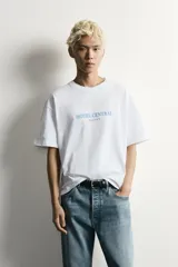Remera blanca de corte relaxed fit con cuello redondo y manga corta. Presenta un estampado frontal en color celeste con el texto "HOTEL CENTRAL" acompañado de cinco estrellas.