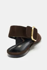 Zapato plano destalonado de ante color marrón oscuro, con punta fina y tira trasera ajustable con hebilla metálica dorada.