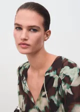 Blusa de gasa con estampado floral en tonos marrón, verde y crudo, escote en V con lazo ajustable y mangas largas con puños abotonados.