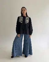 Camisa marrón chocolate con bordado artesanal de flores y hojas en hilo crudo. Presenta cuello con volado, mangas largas con puños abotonados y cierre frontal de botones.
