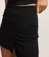 Short pollera negro de bengalina, con superposición asimétrica y corte ajustado. Posee cierre lateral por cremallera invisible y cintura de tiro medio.