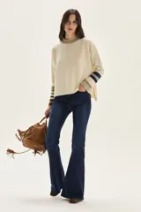 Sweater tejido de lambswool color beige, con cuello redondo y puños acampanados con rayas de colores (marrón, mostaza, bordó y beige). Incluye un detalle de temporada hecho a mano en la espalda.