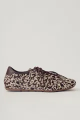Zapatilla deportiva de mujer, modelo Champion Vane, con estampado animal print (vaca/manchas) en tonos marrón y beige. Presenta cordones marrones y detalles de cuero marrón liso en el talón. La suela es delgada y de color marrón claro.