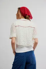 Camisa crop de encaje floral semitransparente, color blanco, con mangas cortas y ribetes en color contrastante.