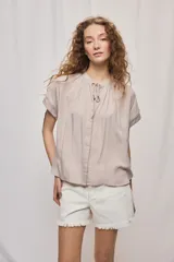 Camisa de manga corta color celeste, confeccionada en viscosa fluida, con silueta amplia y escote redondo con frunces y lazo para anudar.