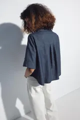 Camisa crop color blanco confeccionada en mezcla de lino, con cuello solapa, escote en pico, mangas cortas con trabilla, bolsillos de plastrón en el pecho y cierre frontal con botones.