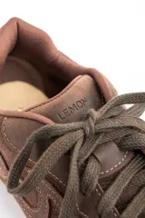 Zapatilla de estilo urbano confeccionada en cuero legítimo y gamuza en tono marrón, con diseño de costuras decorativas laterales y suela plana de goma.