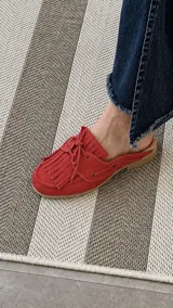 Zueco de cuero color azul marino, con diseño tipo mocasín destalonado, detalles de flecos en el empeine, cordones ajustables y plantilla en tono suela.