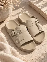 Sandalias de gamuza color tostado, de diseño abierto con tira ancha en el empeine decorada con una hebilla metálica y flecos colgantes.