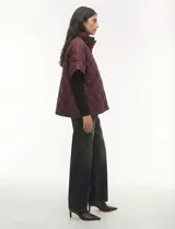 Poncho acolchado color vino tinto, con cuello alto y cierre frontal parcial. Presenta un patrón de costuras capitoné en forma de hoja o diamante y bolsillos delanteros.