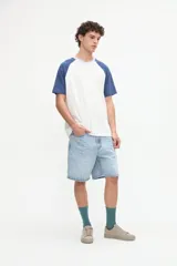 Remera de manga corta estilo raglán, color blanco en el cuerpo con mangas y cuello en tono azul. Presenta un pequeño bordado en el pecho.