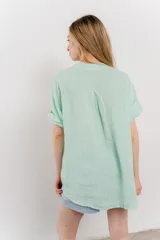 Blusa blanca de lino con escote en V abotonado y mangas cortas arremangadas.