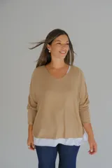 Sweater de punto color camel con diseño de doble capa, escote en V con detalle de vivo plateado y mangas largas. El diseño presenta un bajo asimétrico con una capa inferior blanca visible.