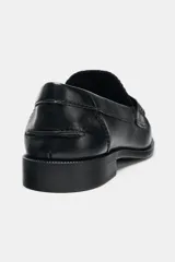 Mocasín plano negro de cuero liso, con antifaz, copete subido y detalle de fruncidos en la parte delantera. Punta redonda y suela de 2,5 cm de altura.