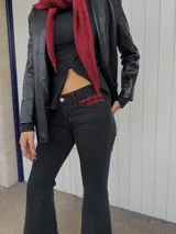 Jean de tiro bajo con calce ajustado en la parte superior y corte flare en la parte inferior. Presenta costuras con pespuntes en color rojo y detalle de bordado en el bolsillo delantero.