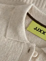 Sweater de punto color beige, con cuello polo y cierre frontal de tres botones, mangas largas con puños acanalados y diseño clásico.