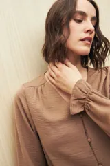 Camisa negra de manga larga con escote en V y botones forrados al tono en el frente. Destaca por su textura sutil y por el detalle de frunces con volados en la parte inferior.